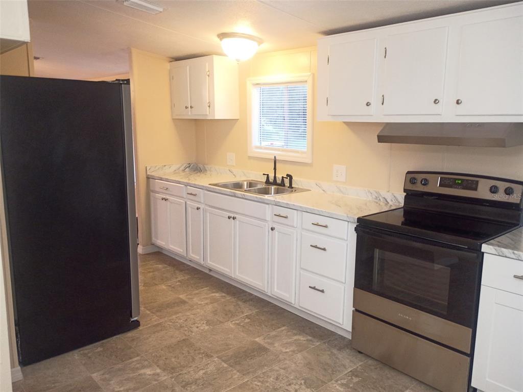 A kitchen features white cabinets, marble-look countertops, a black refrigerator, and a stainless steel stove — 6910 BROOKRIDGE TRAIL, LAKELAND, FL