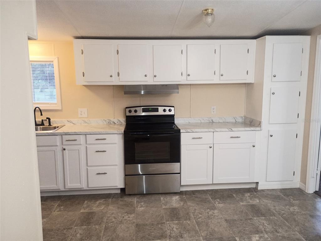 A kitchen with white cabinets, a stainless steel stove, and marble-patterned countertops — 6910 BROOKRIDGE TRAIL, LAKELAND, FL