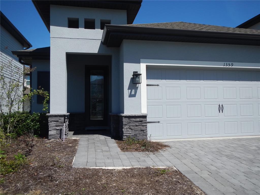 A gray house exterior features a stone-accented entryway, a paved walkway, and a garage — 1359 GREENFIELD LOOP, KISSIMMEE, FL