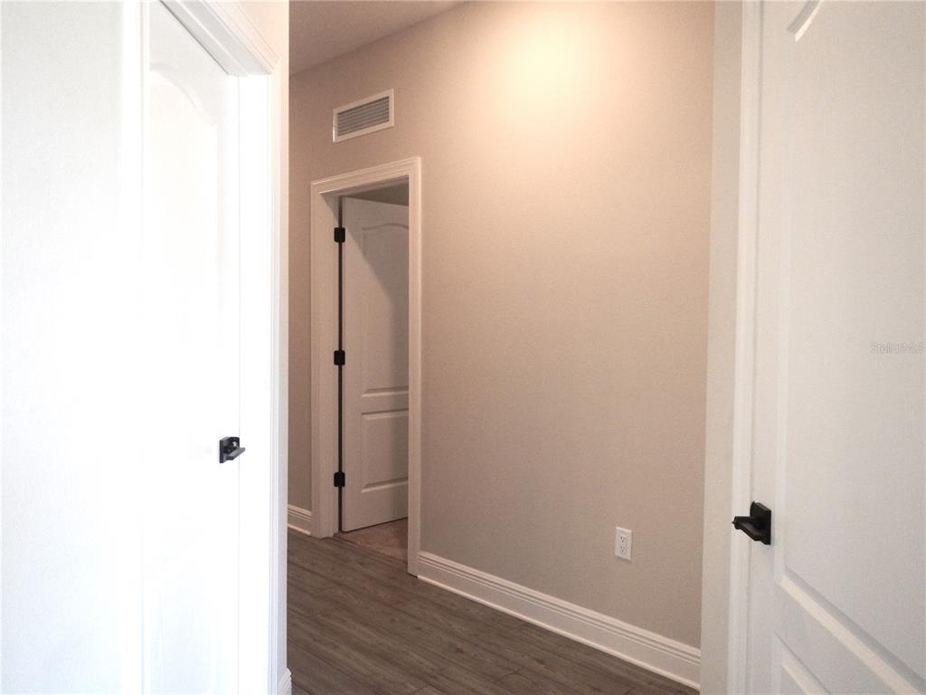 A hallway with light-colored walls, wood-look flooring, and white doors with black hardware — 1359 GREENFIELD LOOP, KISSIMMEE, FL