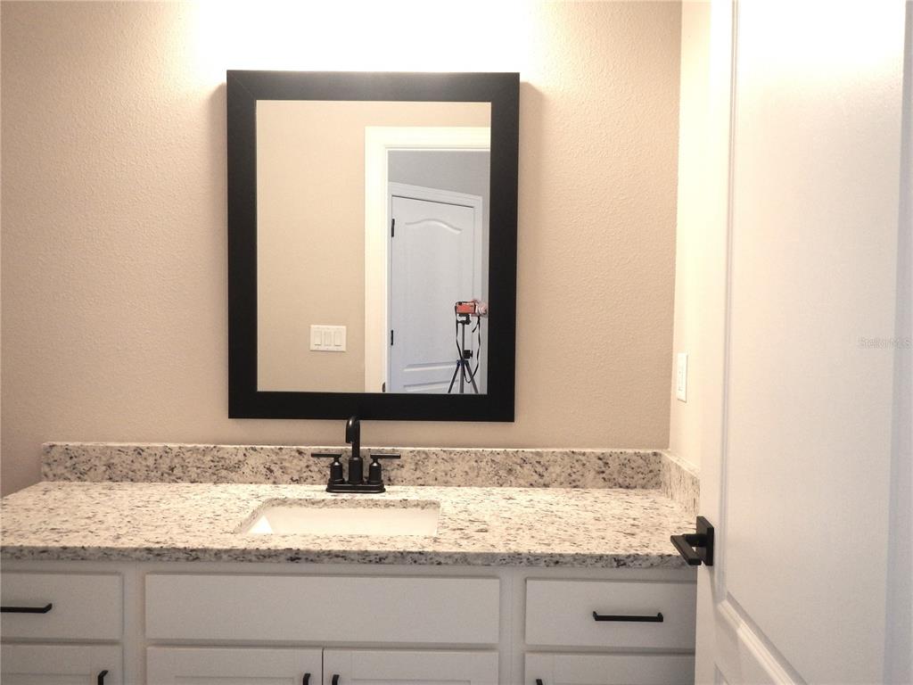 A bathroom vanity features a white cabinet, granite countertop, black faucet, and a framed mirror — 1359 GREENFIELD LOOP, KISSIMMEE, FL
