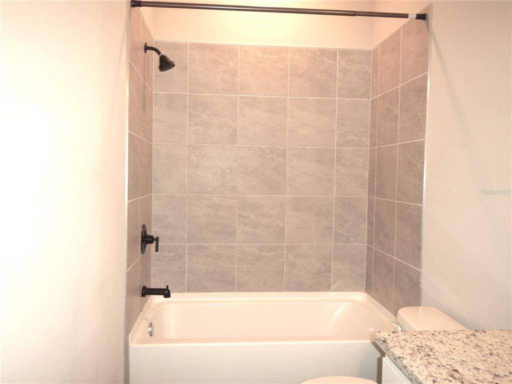 A bathroom features a white bathtub with gray tiled walls and black plumbing fixtures — 1359 GREENFIELD LOOP, KISSIMMEE, FL