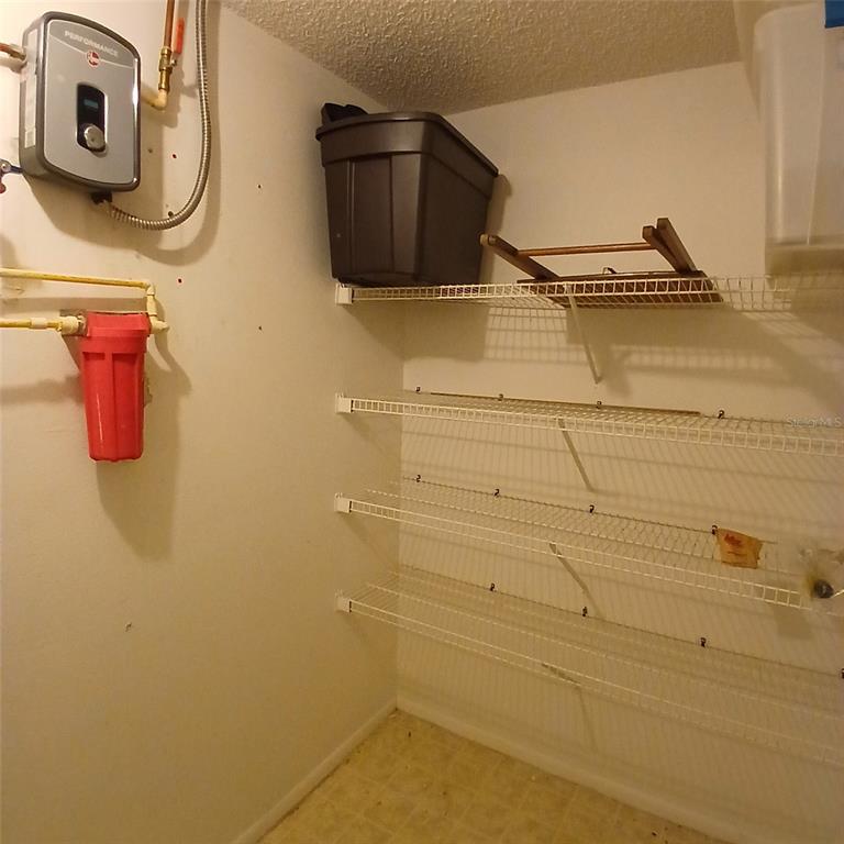 A utility closet featuring wire shelving, a water heater, and a red water filtration system — 9362 NAKOMA WAY, WEEKI WACHEE, FL