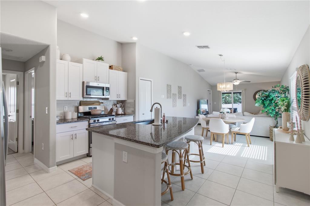 A kitchen with white cabinets, granite countertops, and an island with stools overlooks a dining area — 10331 BLUE PLUME COURT, RIVERVIEW, FL