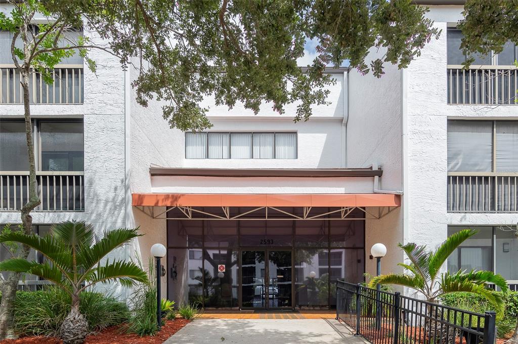 The exterior of a multi-story apartment building features a glass entrance under an orange awning — 2593 COUNTRYSIDE BOULEVARD UNIT 7313, CLEARWATER, FL