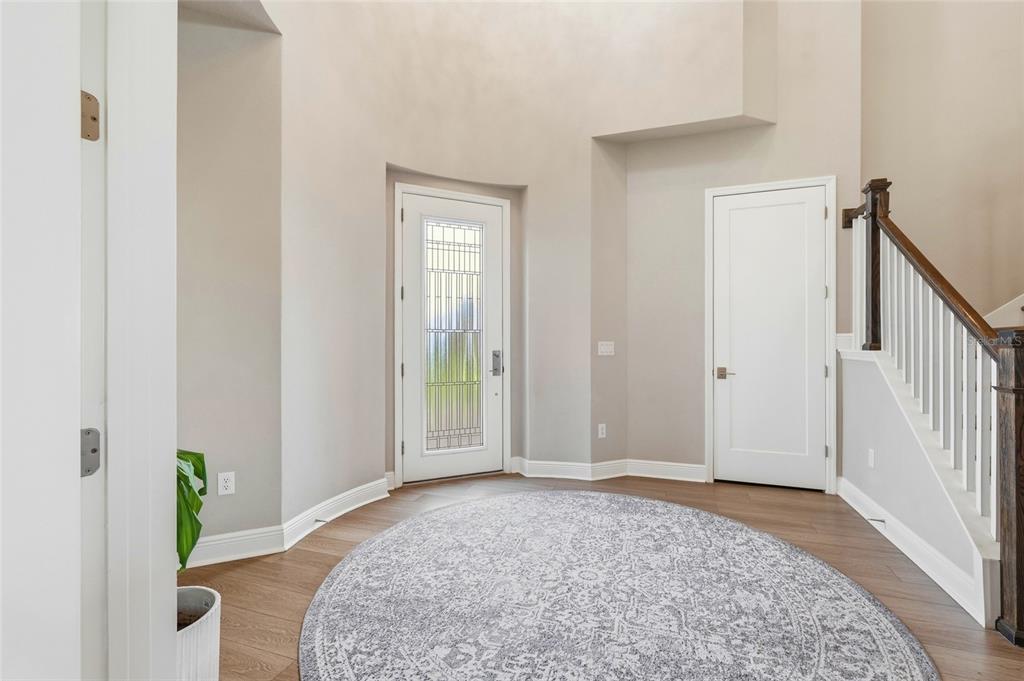 A bright foyer features light-colored walls, wood-look flooring, a round area rug, and a staircase — 8207 RUSHTON PLACE, PARRISH, FL