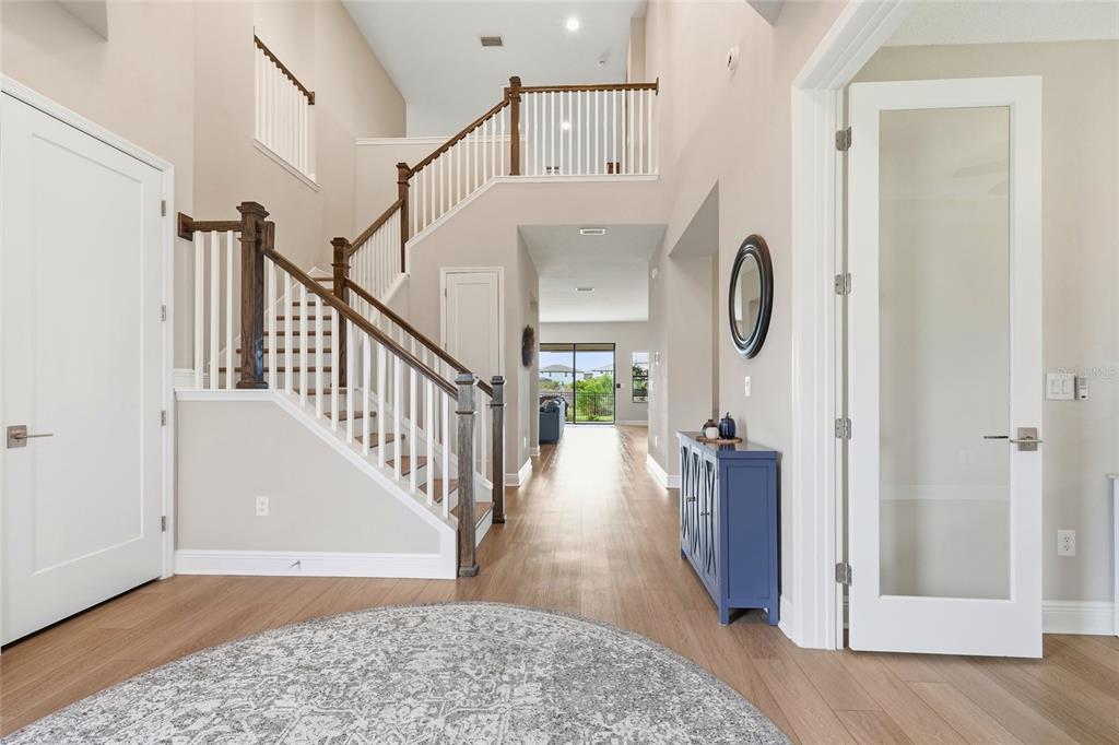 A bright foyer features light wood flooring, a staircase with dark wood railings, and glass-paneled doors — 8207 RUSHTON PLACE, PARRISH, FL