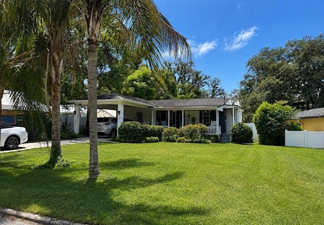 A single-story house with a carport and a large front lawn under a blue sky — 11710 NORTH DRIVE, TAMPA, FL