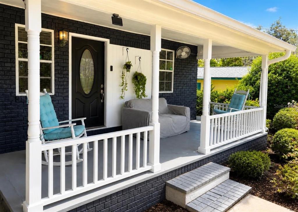 A front porch features dark brick walls, white railings, a black door, and rocking chairs — 11710 NORTH DRIVE, TAMPA, FL