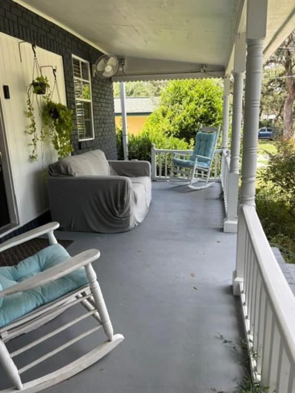 A covered porch features a gray floor, a cushioned loveseat, and two white wooden rocking chairs — 11710 NORTH DRIVE, TAMPA, FL