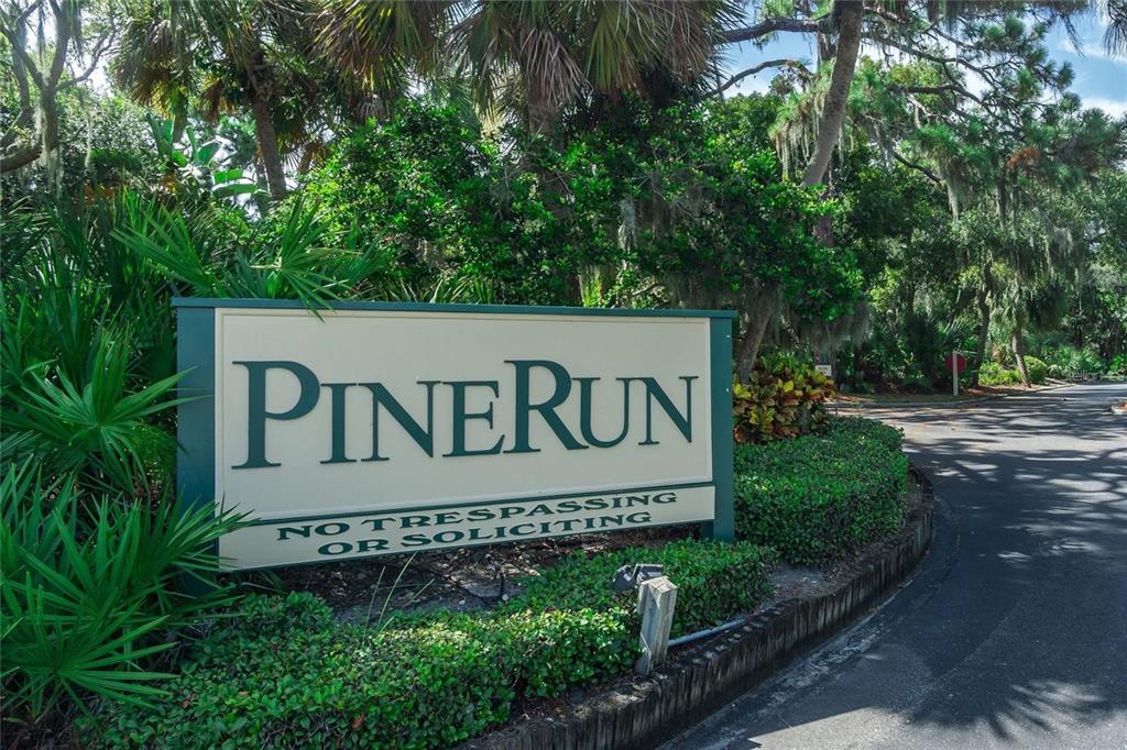 A sign for PineRun stands in a landscaped area next to a paved road — 101 WOODLAND PLACE, OSPREY, FL
