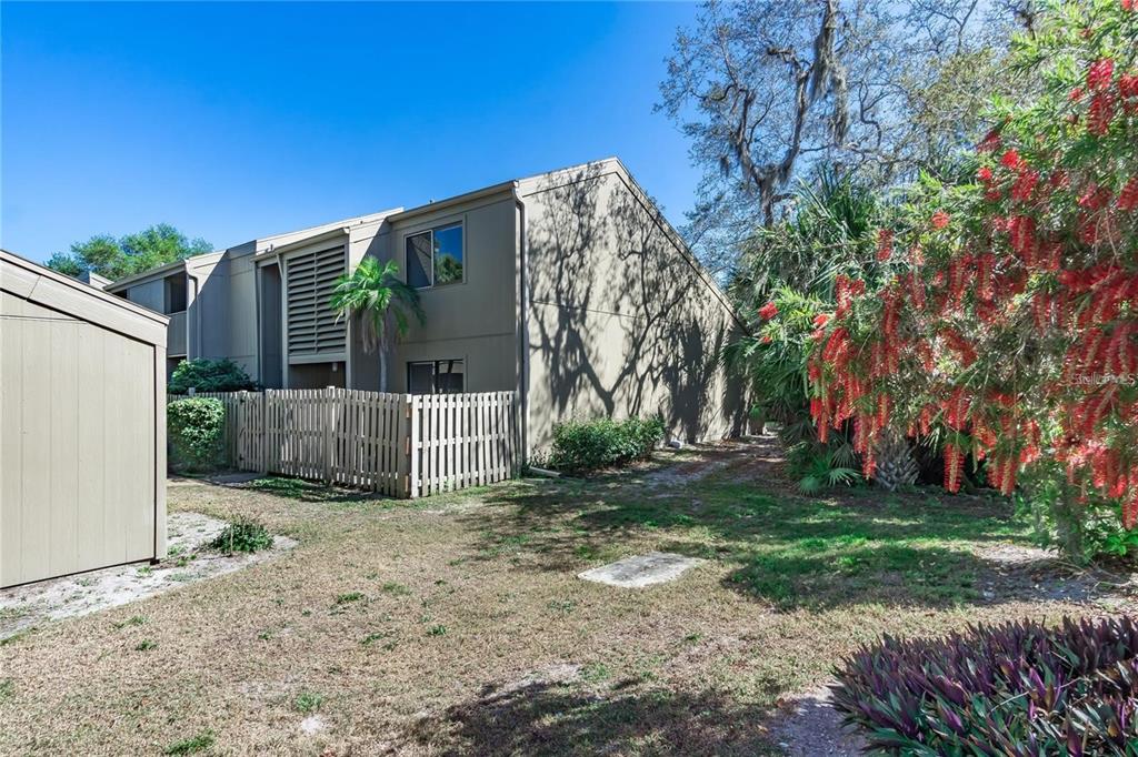 Exterior view of a multi-story tan townhouse with a fenced patio and surrounding landscaping — 101 WOODLAND PLACE, OSPREY, FL