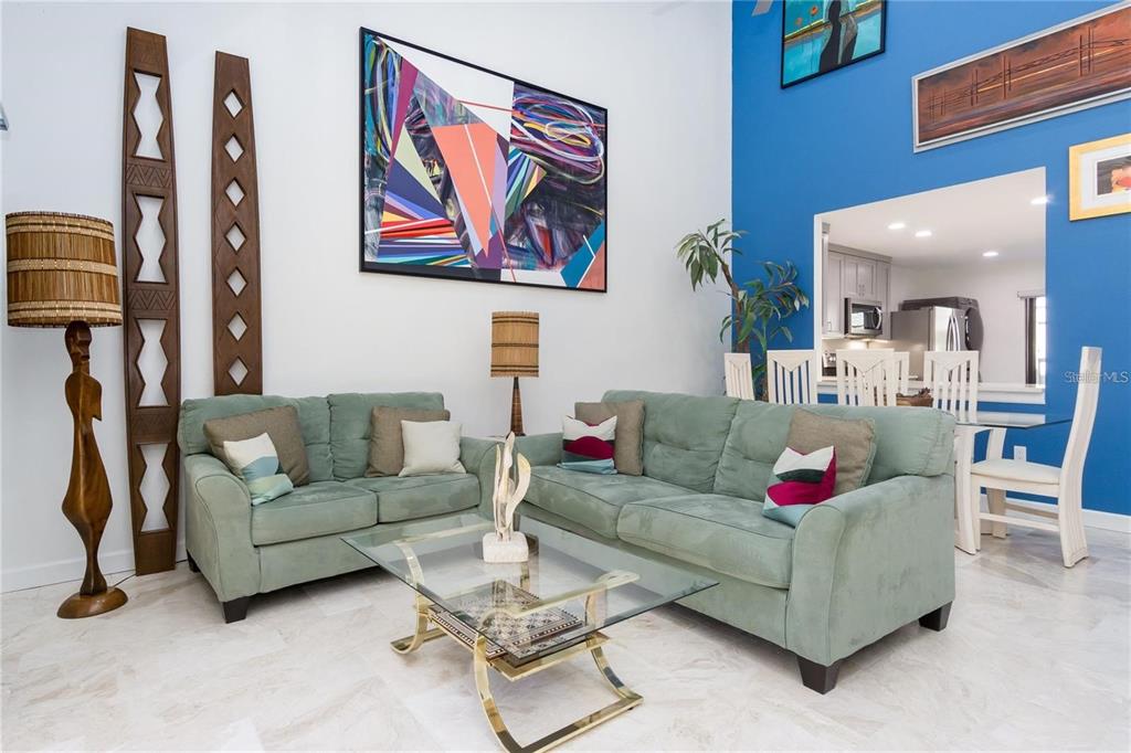 A living room features two sage green sofas, a glass coffee table, and blue accent walls — 101 WOODLAND PLACE, OSPREY, FL