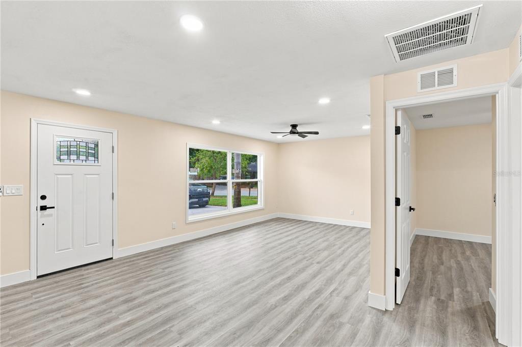 A living room with light-colored walls, gray wood-look flooring, a ceiling fan, and front door — 1105 PARK STREET, SEFFNER, FL