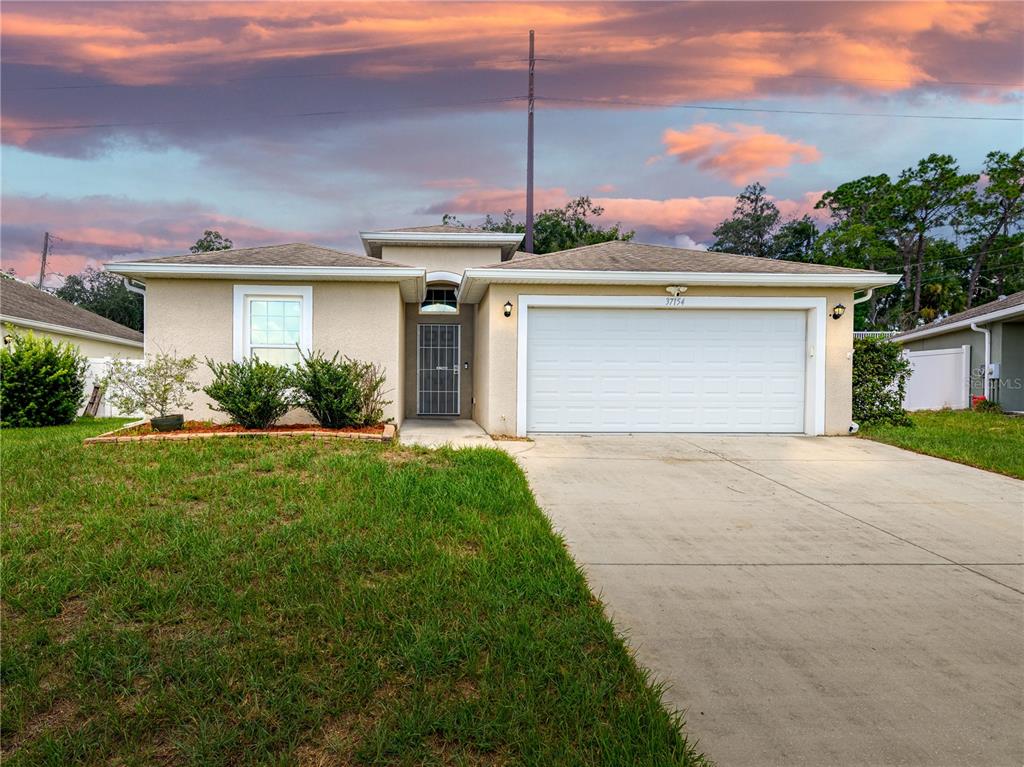 A single-story house with a beige stucco exterior, a two-car garage, and a concrete driveway — 37154 HIGHLAND BLUFF CIRCLE, DADE CITY, FL