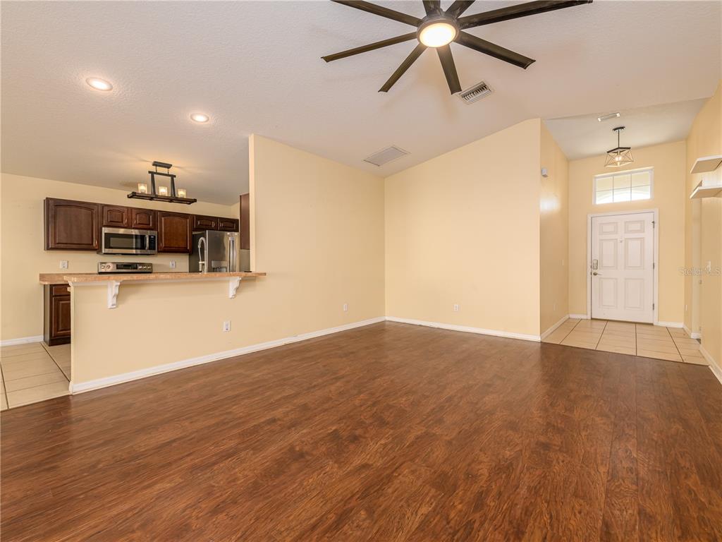 An open-concept living area features wood-look flooring, a kitchen with dark cabinets, and an entryway — 37154 HIGHLAND BLUFF CIRCLE, DADE CITY, FL