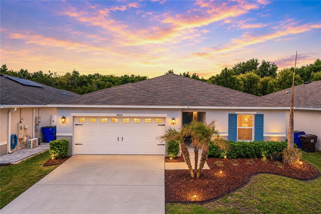 A light blue house exterior features a white garage door, a front porch, and landscaping — 2865 MOSSHIRE CIRCLE, ST CLOUD, FL