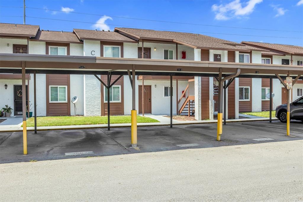 A covered parking area sits in front of a two-story apartment building with brown trim — 39132 COUNTY ROAD 54 UNIT 2066, ZEPHYRHILLS, FL
