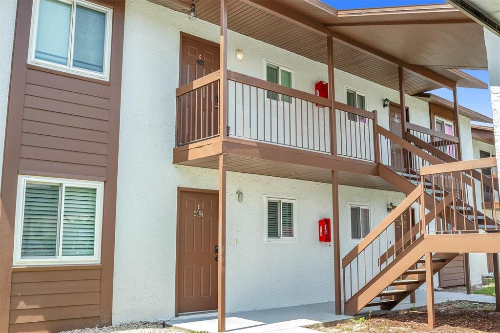 A two-story apartment building exterior features brown trim, a metal staircase, and a balcony — 39132 COUNTY ROAD 54 UNIT 2066, ZEPHYRHILLS, FL