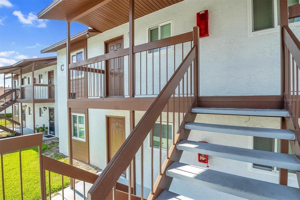 An exterior view of a two-story apartment building with brown railings and concrete stairs — 39132 COUNTY ROAD 54 UNIT 2066, ZEPHYRHILLS, FL