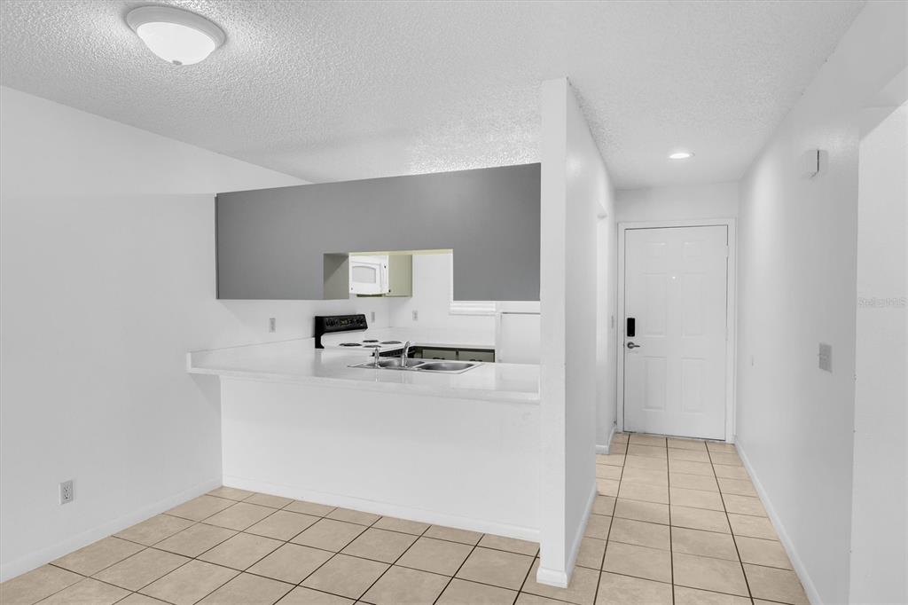 A kitchen with a breakfast bar, white countertops, and tile flooring opens to an entryway — 39132 COUNTY ROAD 54 UNIT 2066, ZEPHYRHILLS, FL