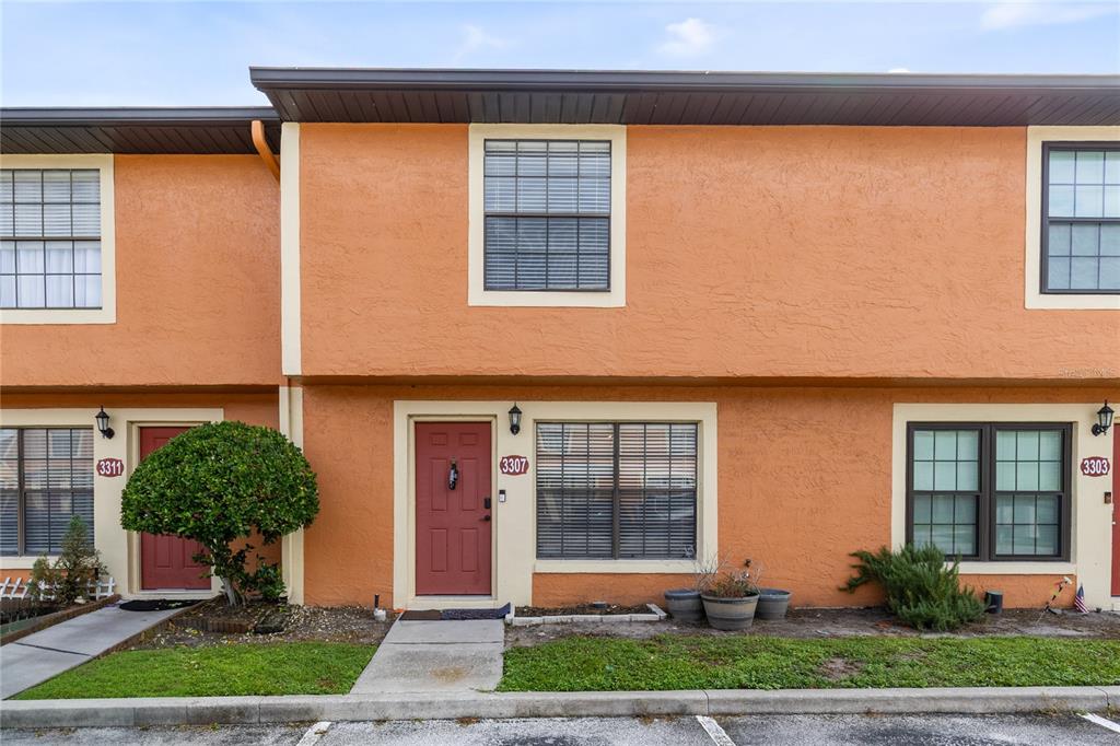 A two-story orange stucco townhouse exterior features a red front door and dark-framed windows — 3307 AMBER WOOD WAY UNIT 106, WINTER PARK, FL