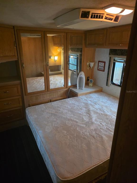 A bedroom in a recreational vehicle featuring a bed, mirrored wardrobes, and overhead storage cabinets — 3000 CLARCONA ROAD UNIT 770, APOPKA, FL