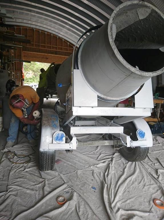 A worker uses a power tool on a concrete mixer inside a metal-roofed workshop — 99999 EASTERN AVENUE, ST CLOUD, FL