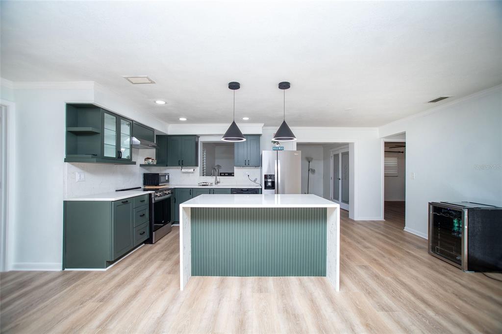 A kitchen features dark green cabinets, a white-topped island, and light wood-look flooring — 989 8TH AVENUE NE, LARGO, FL