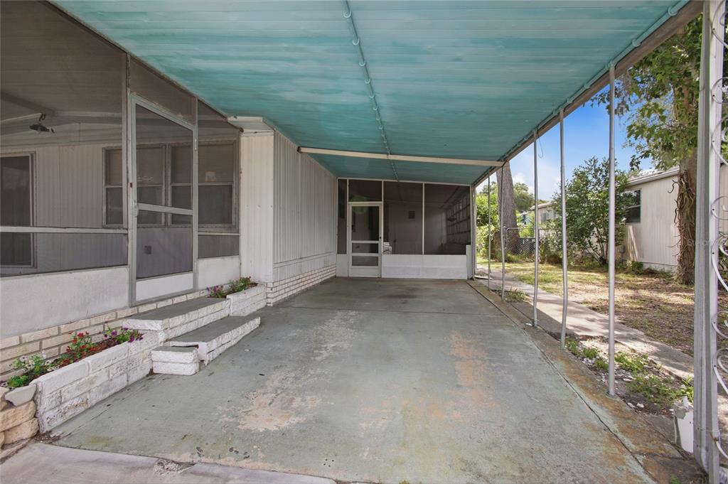 A concrete carport with a blue metal roof leads to a screened-in porch entrance — 110 MAPLE DRIVE, DEBARY, FL