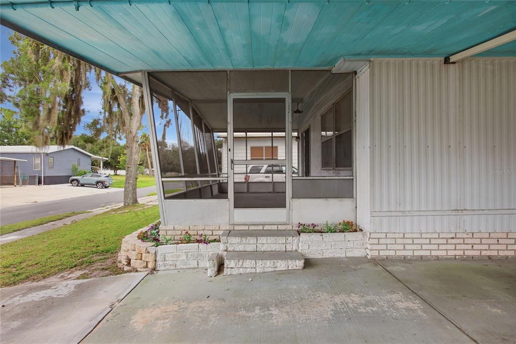 A screened-in porch with concrete steps sits under a carport next to a mobile home — 110 MAPLE DRIVE, DEBARY, FL