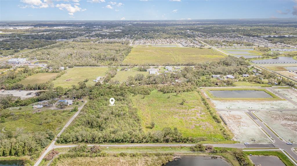 An aerial view shows a vacant, wooded lot marked with a location pin near residential development — 12TH STREET SE, RUSKIN, FL