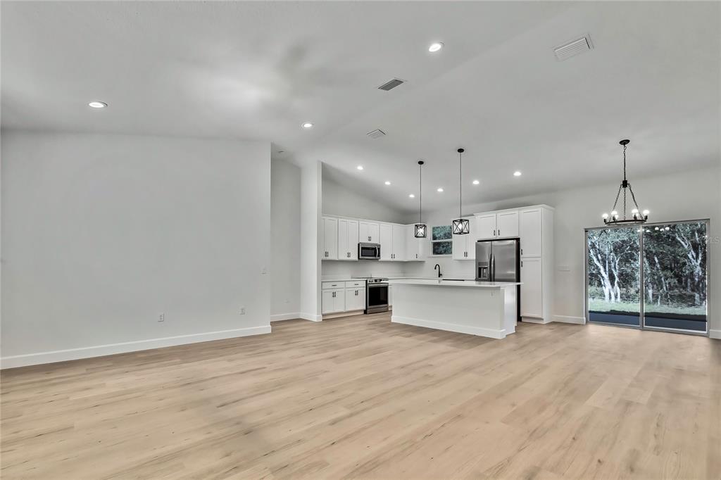 An open-concept kitchen and living area features white cabinetry, stainless steel appliances, and wood flooring — 8118 N SANTOS DRIVE, CITRUS SPRINGS, FL