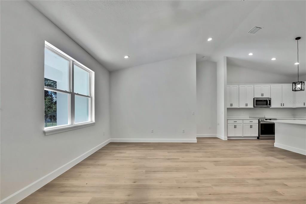 An open-concept room features light wood-look flooring, white walls, and an adjacent modern kitchen — 8118 N SANTOS DRIVE, CITRUS SPRINGS, FL