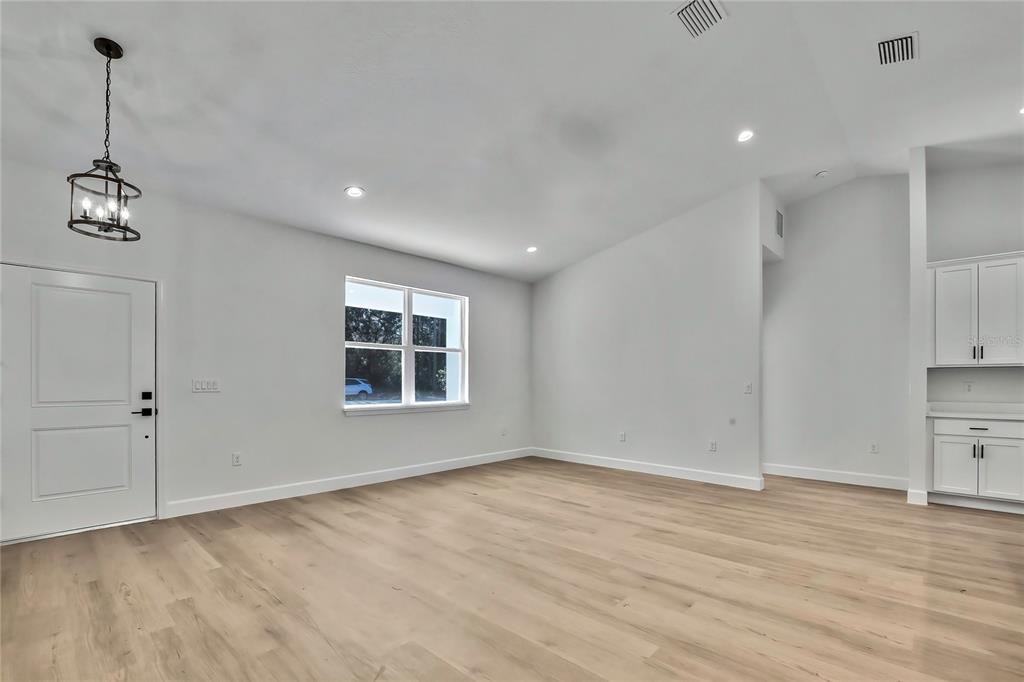 A bright, empty room features light wood-look flooring, white walls, a window, and a pendant light — 8118 N SANTOS DRIVE, CITRUS SPRINGS, FL