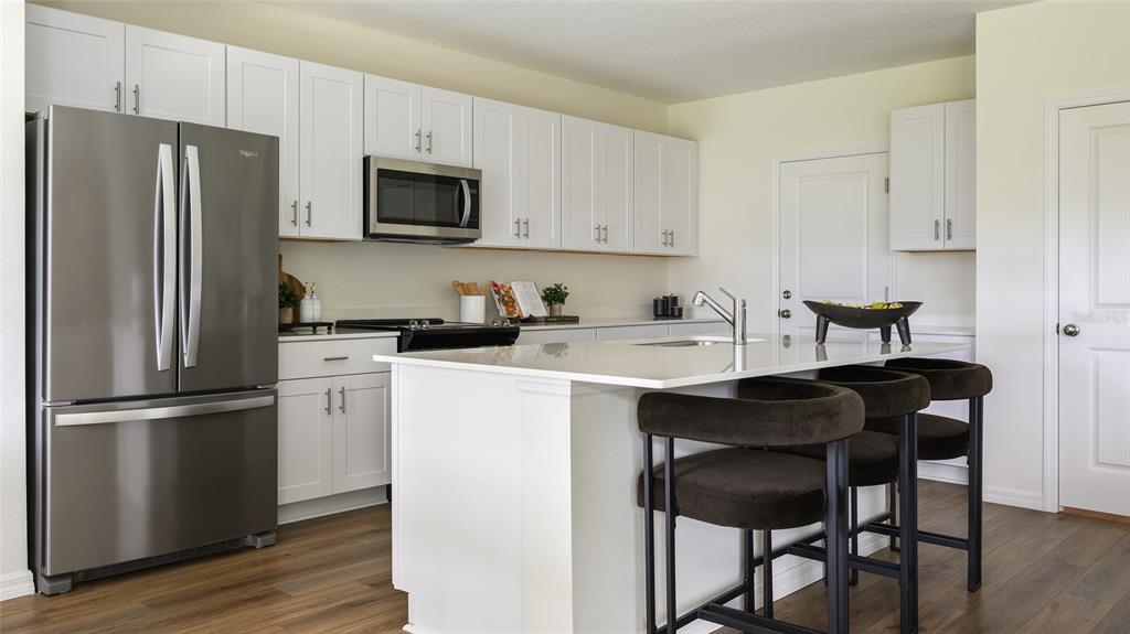 A modern kitchen features white cabinetry, stainless steel appliances, a quartz island, and dark stools — 34620 SILENT PINE RUN, DADE CITY, FL