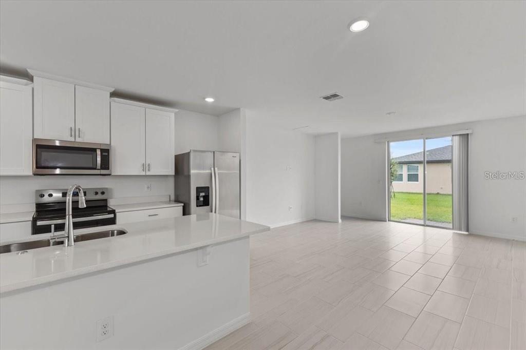 A modern kitchen with white cabinets and quartz countertops opens to a bright living area — 3552 BROADWING BOULEVARD, POINCIANA, FL