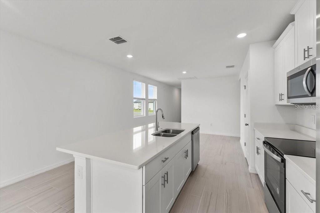 A modern kitchen features white cabinetry, a central island with a sink, and light-colored flooring — 3552 BROADWING BOULEVARD, POINCIANA, FL