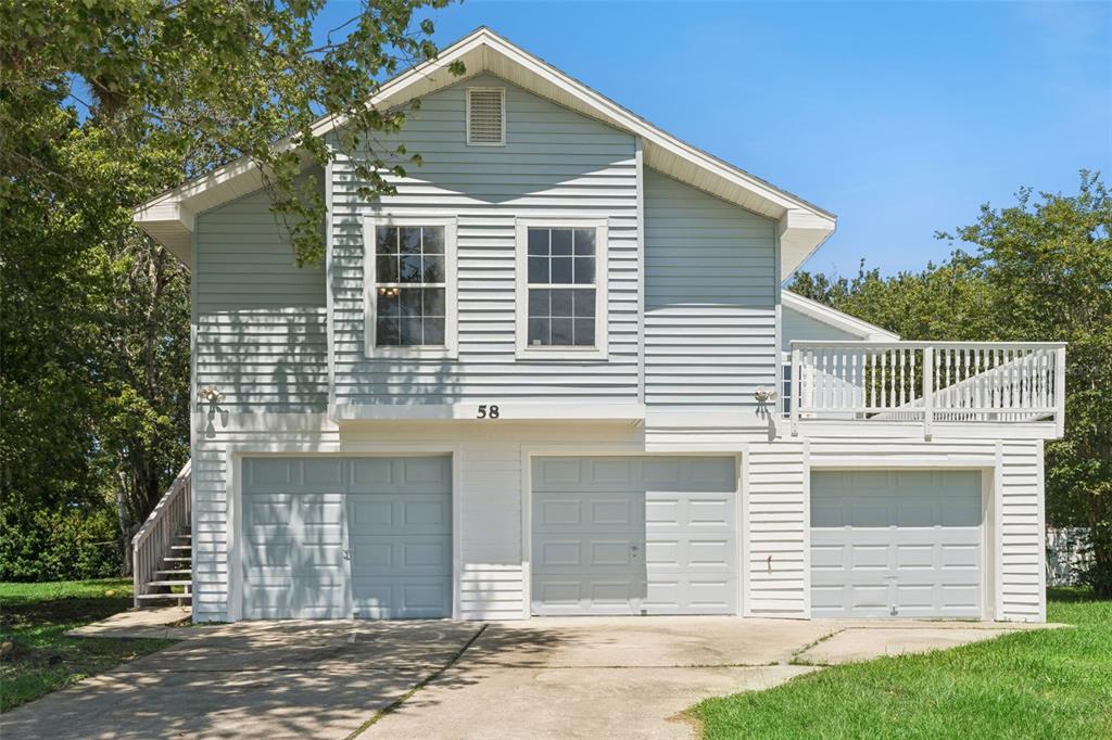 A two-story house with light blue siding, three garage doors, and an elevated side deck — 58 KANKAKEE TRAIL, PALM COAST, FL