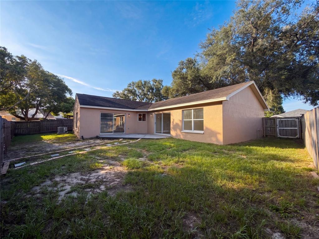 The exterior of a tan house features a concrete patio, sliding glass doors, and grass — 2330 FOGGY RIDGE PARKWAY, LAND O LAKES, FL