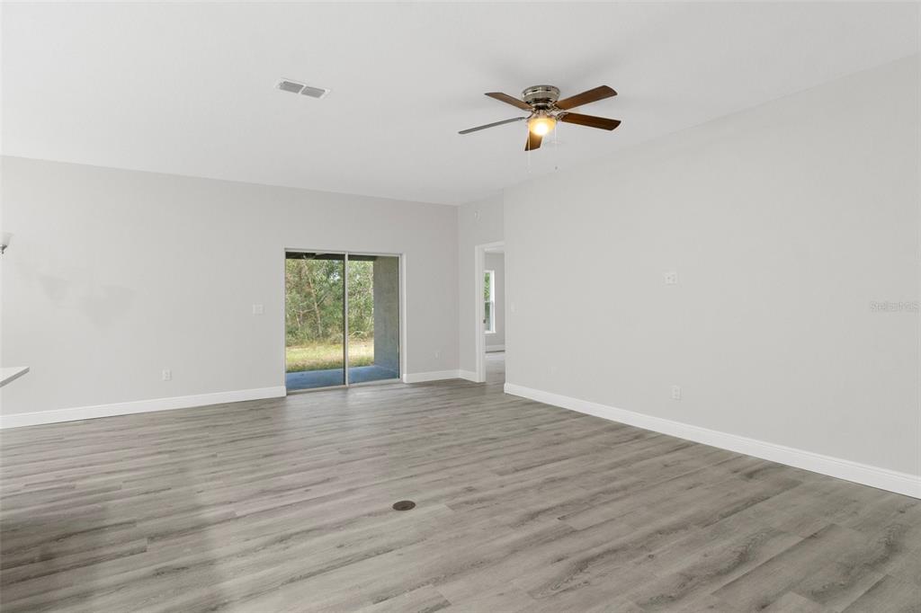 An empty living room features gray wood-look flooring, a ceiling fan, and sliding glass doors — 4855 E PRINCETON LANE, HERNANDO, FL