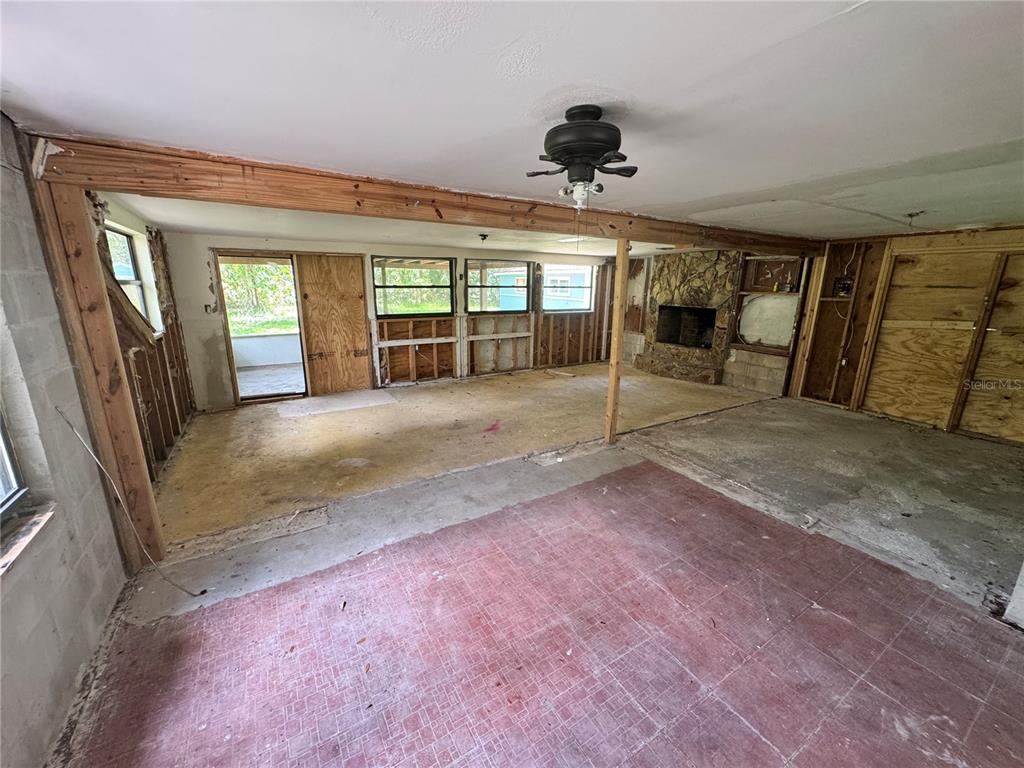 An unfinished room features exposed wall studs, a stone fireplace, and a ceiling fan — 9010 MAIDEN LANE, ARIPEKA, FL