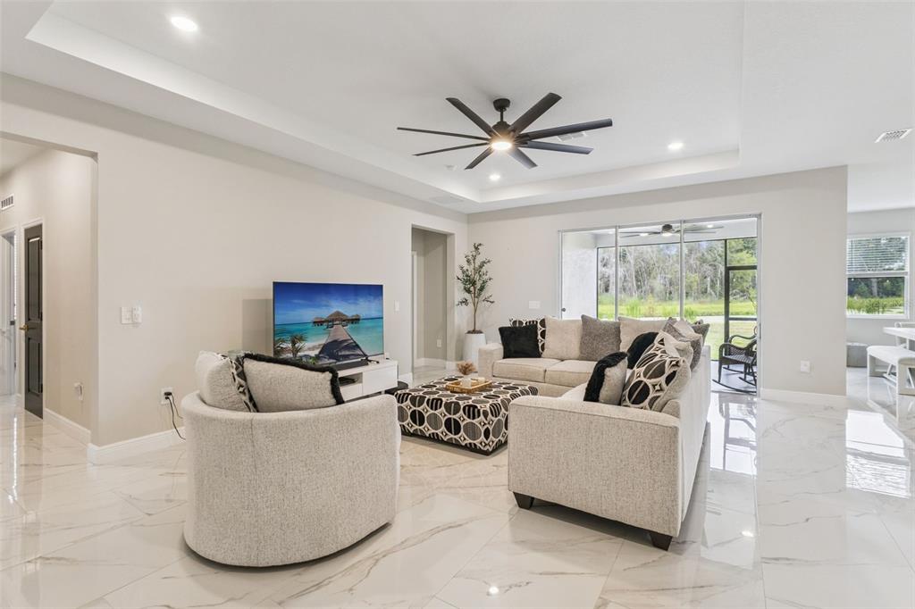 A living room features light tile floors, a tray ceiling, and a view of the outdoors — 5361 DAGENHAM DRIVE, DAVENPORT, FL