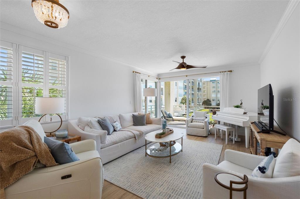 A bright living room features a white sofa, armchairs, a piano, and a glass coffee table — 7912 SAILBOAT KEY BOULEVARD S UNIT 201, SOUTH PASADENA, FL