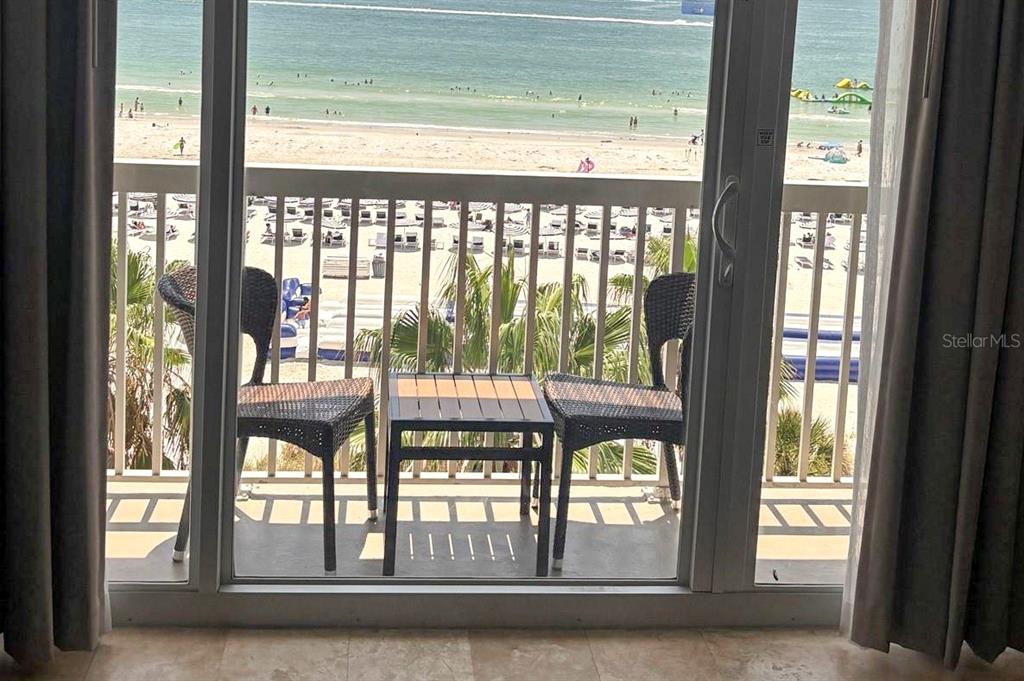 A balcony with two chairs and a small table overlooks a sandy beach and ocean — 5500 GULF BOULEVARD UNIT 7221, ST PETE BEACH, FL