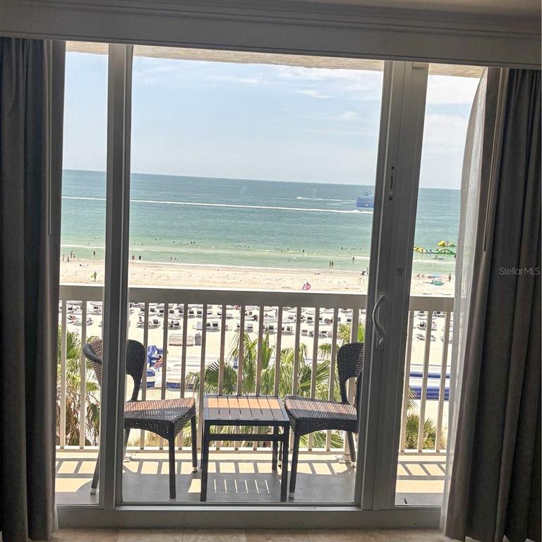 A balcony with two chairs and a table overlooks a sandy beach and the ocean — 5500 GULF BOULEVARD UNIT 7221, ST PETE BEACH, FL