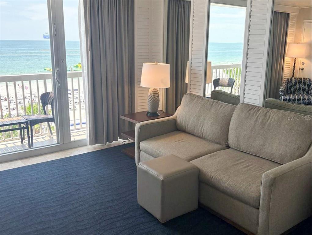 A living room features a sofa, ottoman, and sliding glass doors overlooking the ocean — 5500 GULF BOULEVARD UNIT 7221, ST PETE BEACH, FL