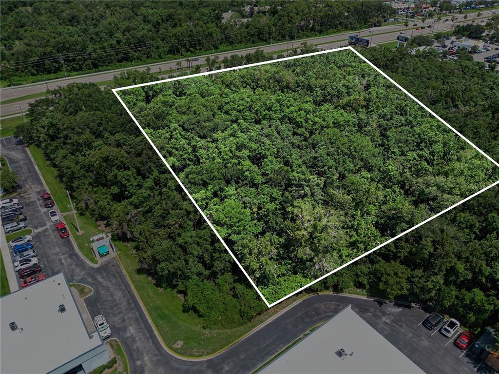 An aerial view shows a rectangular, wooded plot of land bordered by parking lots and roads — 6000 S SEMORAN BOULEVARD, ORLANDO, FL