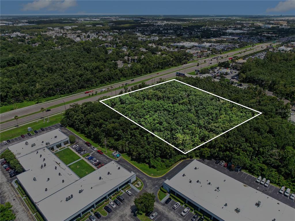 An aerial view shows a wooded, rectangular plot of land outlined in white near commercial buildings — 6000 S SEMORAN BOULEVARD, ORLANDO, FL