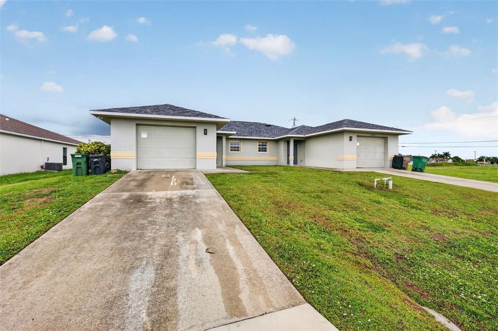A single-story duplex with two garages and concrete driveways under a blue sky — 1223/1225 NE 15TH LANE, CAPE CORAL, FL